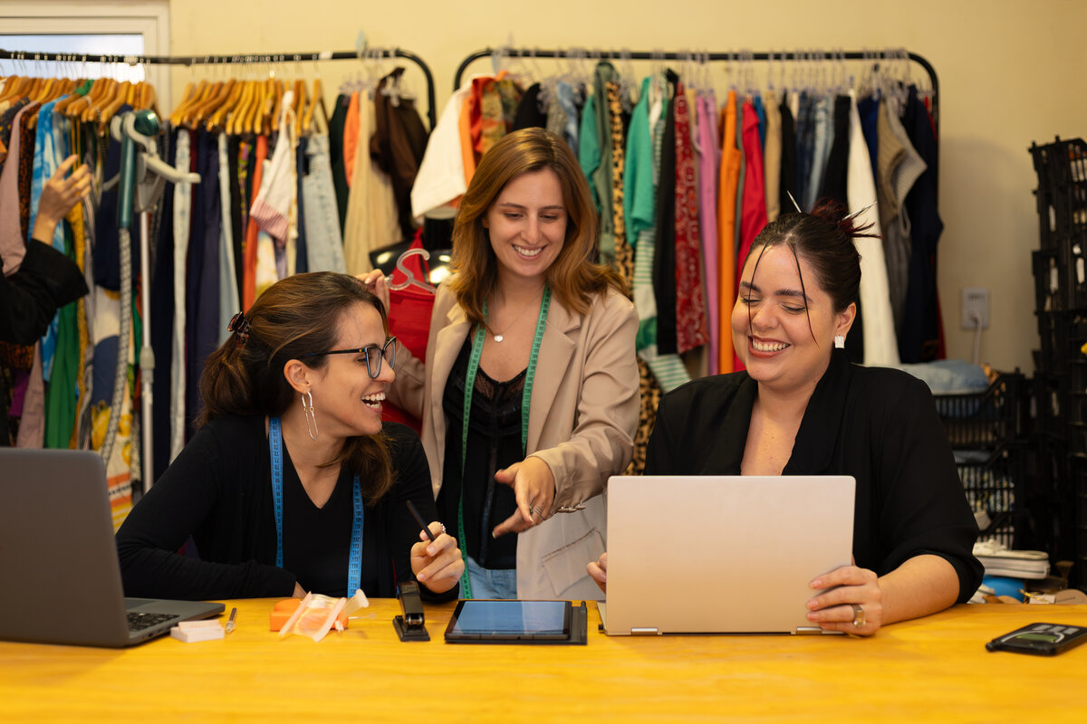 Equipe da Susy e da Susclo trabalhando juntas com laptop e tablet no balcão do brechó